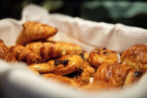 Una cesta con varios pasteles, incluyendo croissants y muffins, sobre una superficie blanca.