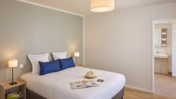 A modern hotel room with a large bed, bedside lamps, a reading light, a magazine, and a hat on the bed.