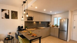 A modern kitchen with a central island, stainless steel appliances, and a dining area with a green chair. - Esperanza Grand Apartments II • Marbella Centro (Marbella)
