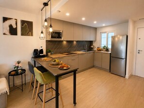 Une cuisine moderne dotée d’un îlot central, d’appareils électroménagers en acier inoxydable et d’un coin repas avec une chaise verte.