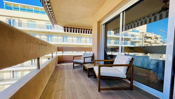 A balcony with wooden flooring, two wooden chairs, and a large window offering a view of other buildings. - Esperanza Grand Apartments I • Marbella Center (Marbella)