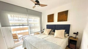 A bedroom with a bed, a ceiling fan, a nightstand, and a view of the outside balcony. - Esperanza Grand Apartments I • Marbella Center (Marbella)