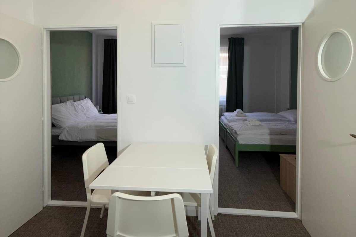 A compact room with a white table and chairs, two single beds, and a small white-framed picture on the wall.