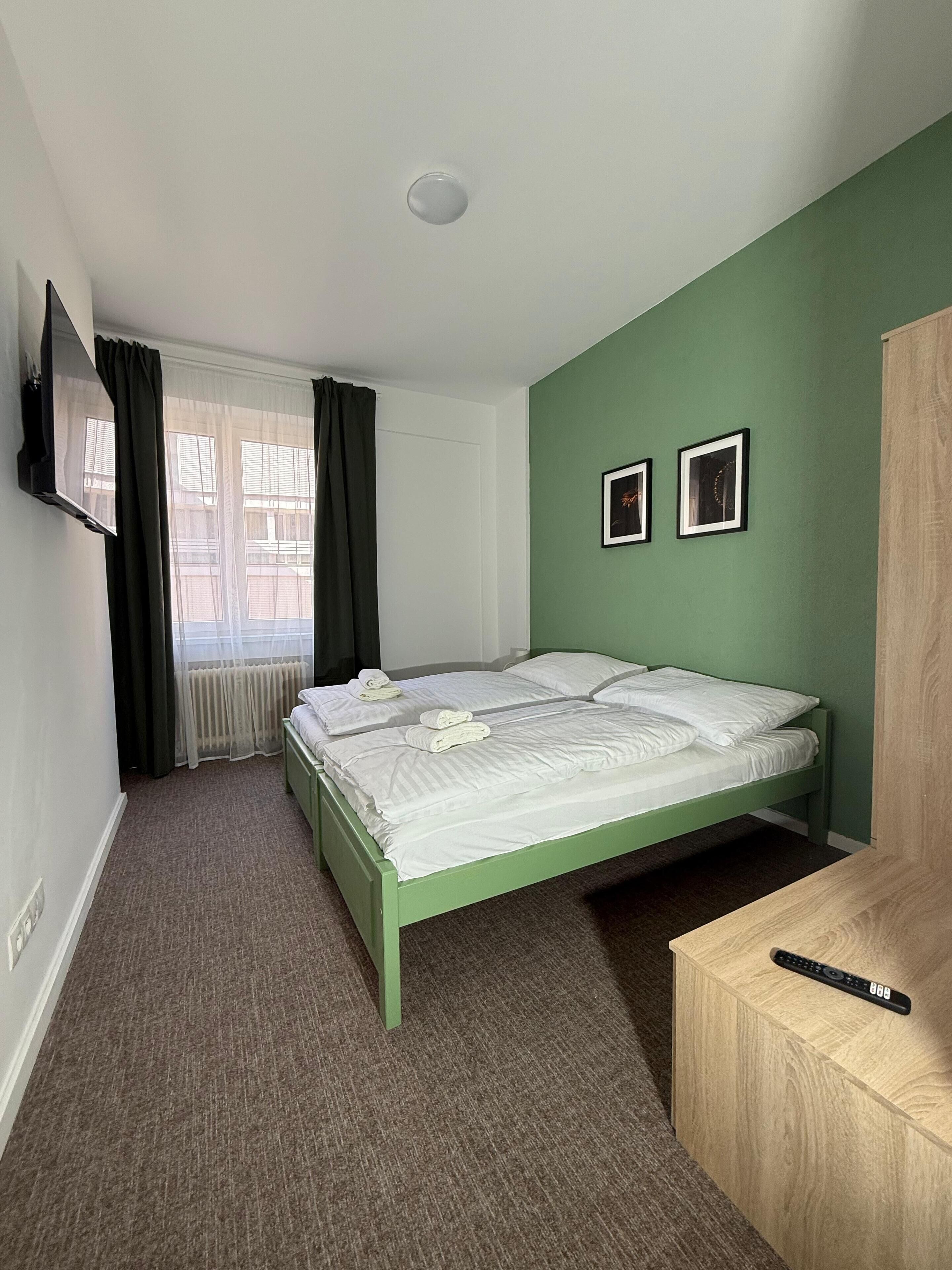 Una camera da letto con una parete verde, un letto con biancheria bianca, una scrivania in legno e un televisore montato a parete.