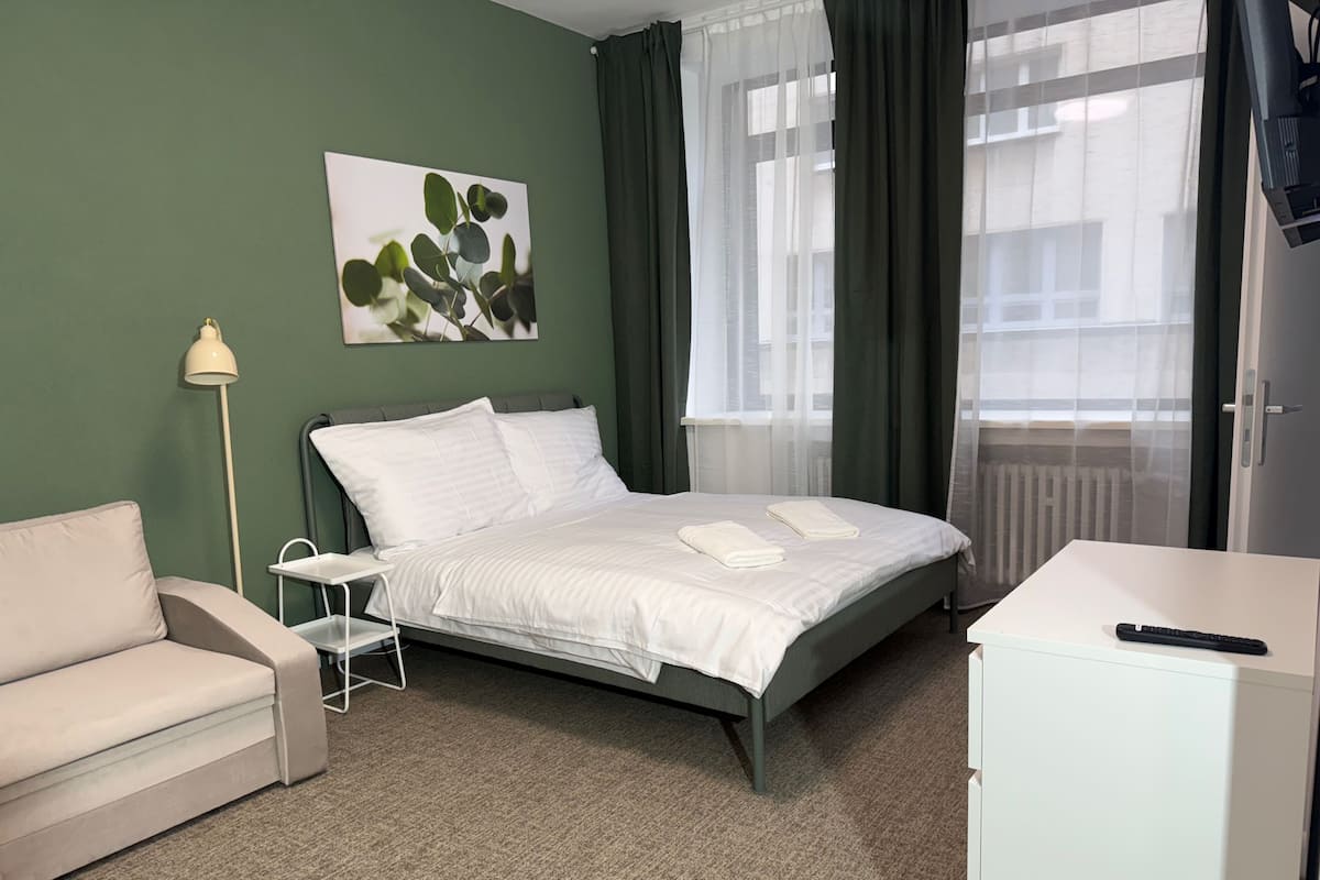A hotel room with a bed, a sofa, a desk, and a window with curtains.