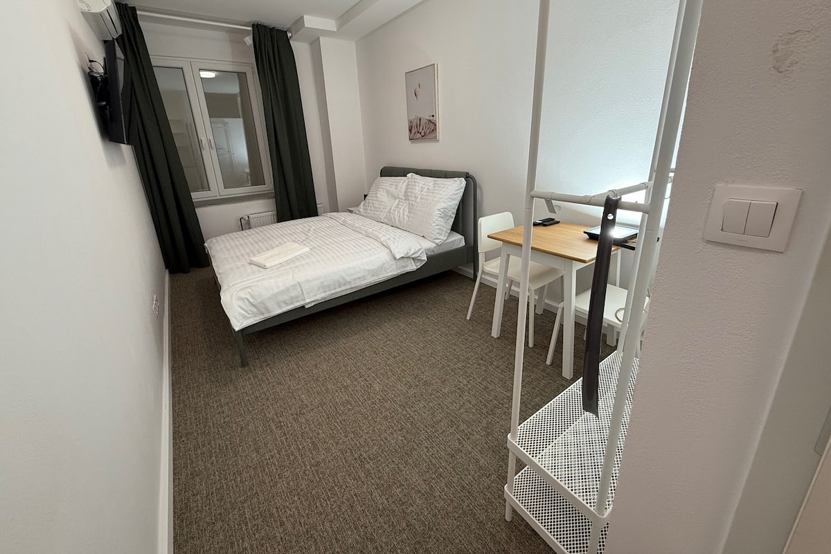 A small, neatly arranged bedroom with a bed, a desk, and a chair.