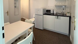 A compact kitchen with white appliances, a dining table with chairs, and a small countertop with a microwave and kettle. - Gremium Apartments (Bratislava)