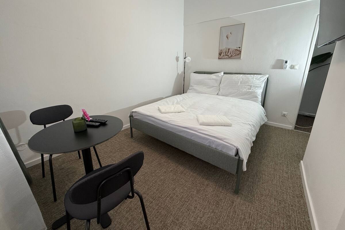 A hotel room with a bed, a round table with chairs, a small desk, and a wall-mounted phone.