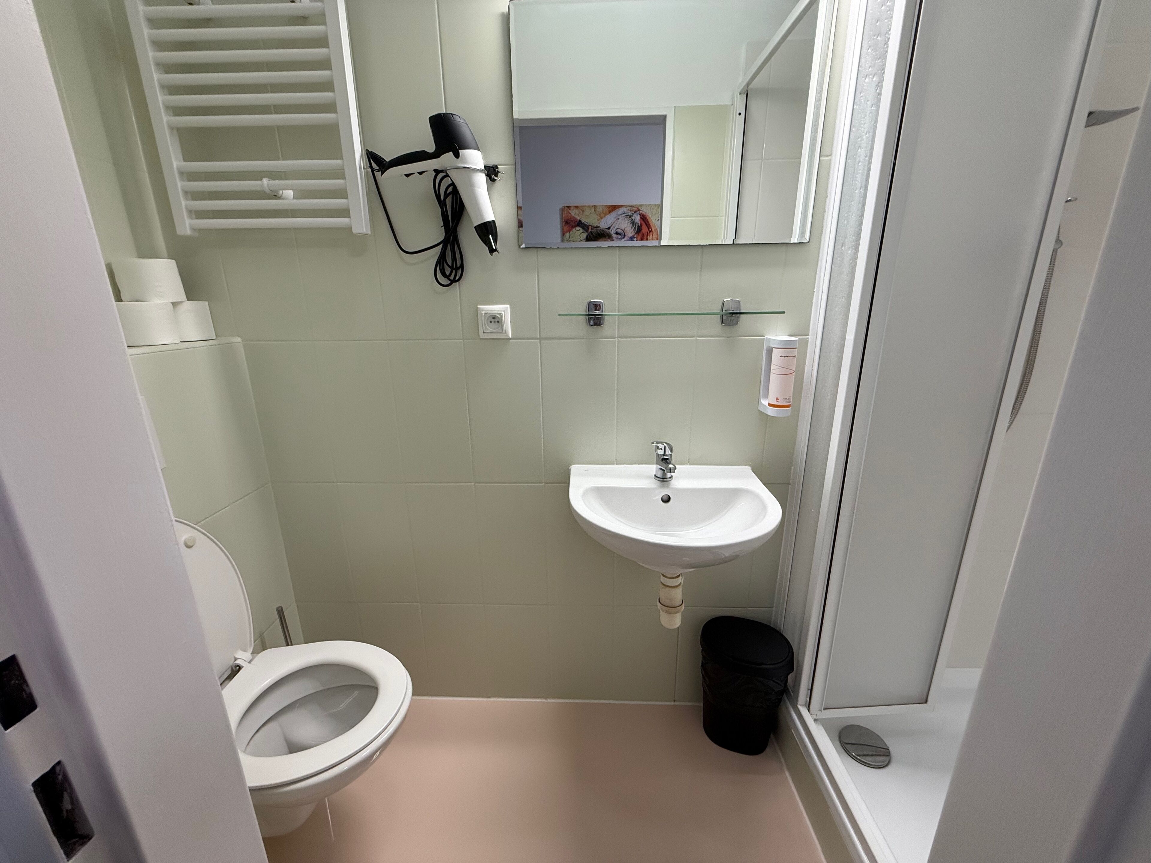 A compact bathroom with a toilet, sink, and a hairdryer mounted on the wall.