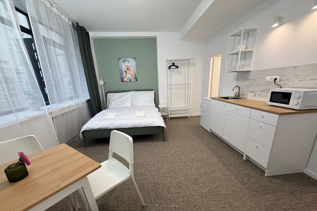 A hotel room with a bed, a desk, a chair, a microwave, and a small kitchen area.