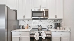 A modern kitchen with white cabinets, a stainless steel refrigerator, a microwave, a gas stove, and a coffee machine. - The Epic 00403 Vista Cay Resort Orlando Florida (Orlando)
