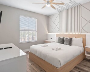 A modern bedroom with a wooden bed frame, a white bedside table, a nightstand, and a ceiling fan.