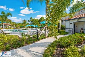 A resort pool area with lounge chairs, umbrellas, and palm trees.