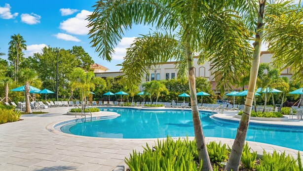A pool area with lounge chairs and umbrellas, surrounded by palm trees and a building in the background. - The Epic 00403 Vista Cay Resort Orlando Florida (Orlando)