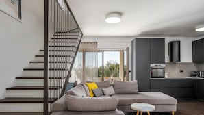 A modern living room with a grey sectional sofa, a small round table, and a staircase with a black railing. - Villa Casa Venus with pool in Istria, for 6 guests, quiet location, near Porec (Višnjan)