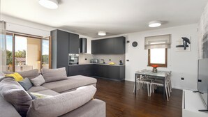 A modern living space with a grey sofa, a dining table with chairs, a kitchen area, and a large window providing natural light. - Villa Casa Venus with pool in Istria, for 6 guests, quiet location, near Porec (Višnjan)