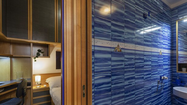 Ein Hotelzimmer mit Bett, Nachttisch, Lampe und Meerblick durch ein Fenster.