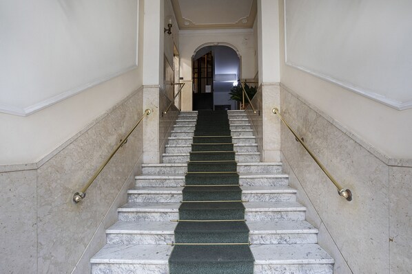 A marble staircase with a green carpet, leading to a doorway.