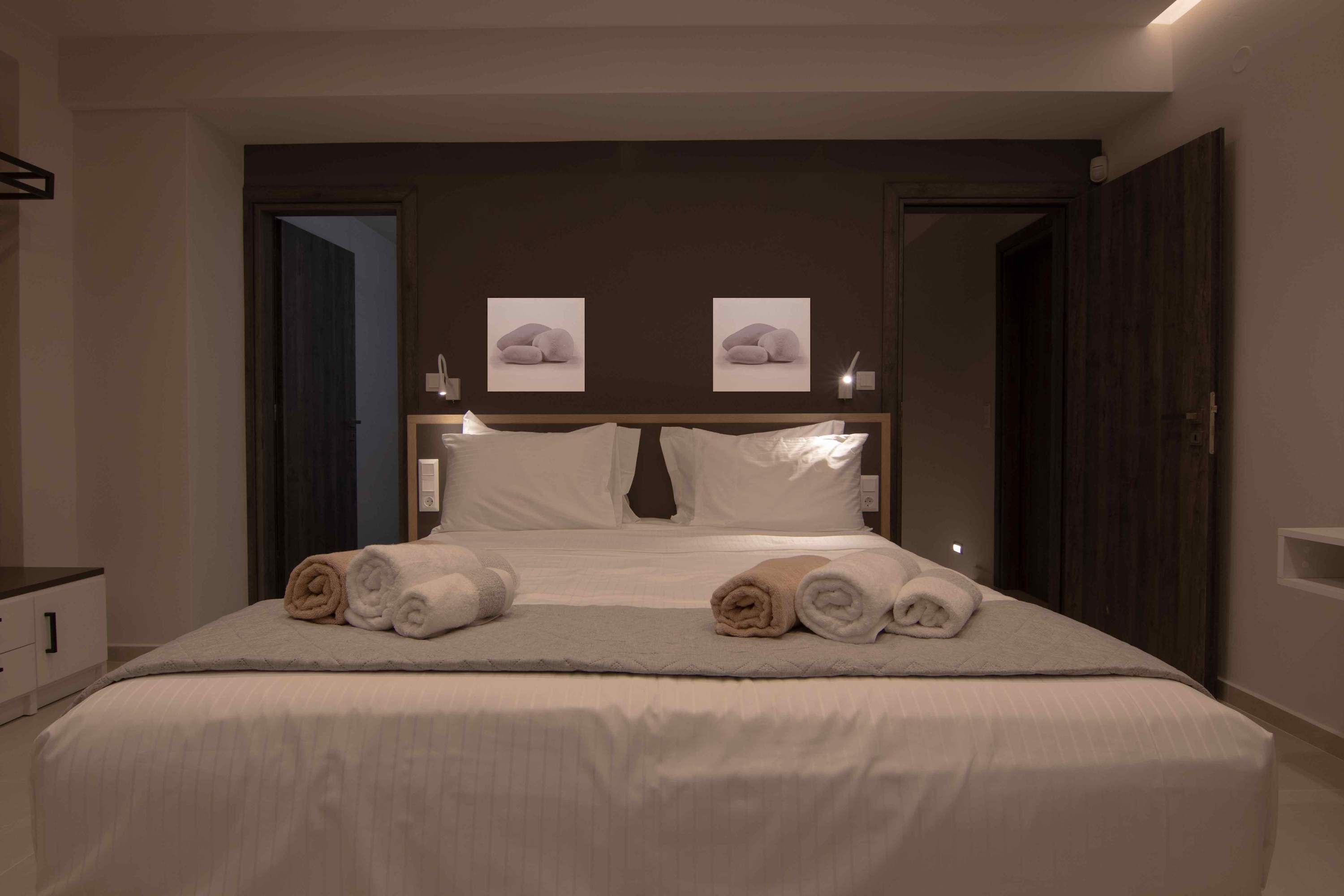 A neatly made bed with rolled towels, a dark headboard, and two framed pictures on the wall.