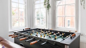 Una mesa de fútbol de mesa en una habitación con ventanas amplias y una planta colgante.