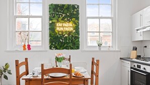 Una cocina moderna con armarios blancos, una mesa de comedor de madera y un letrero de neón en la pared.