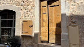 A stone building with a wooden door and shutters, a small window, and a potted plant.