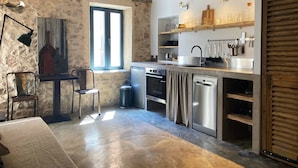 A rustic kitchen with stone walls, a wooden ceiling, and a window. It includes a sink, stove, and various kitchen utensils.