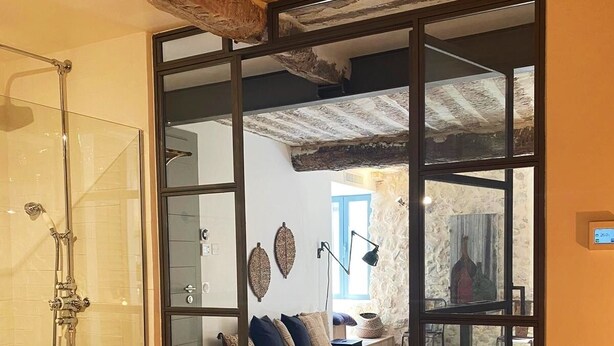 A room with a bed, a glass shower enclosure, and a view through a glass door to another room.