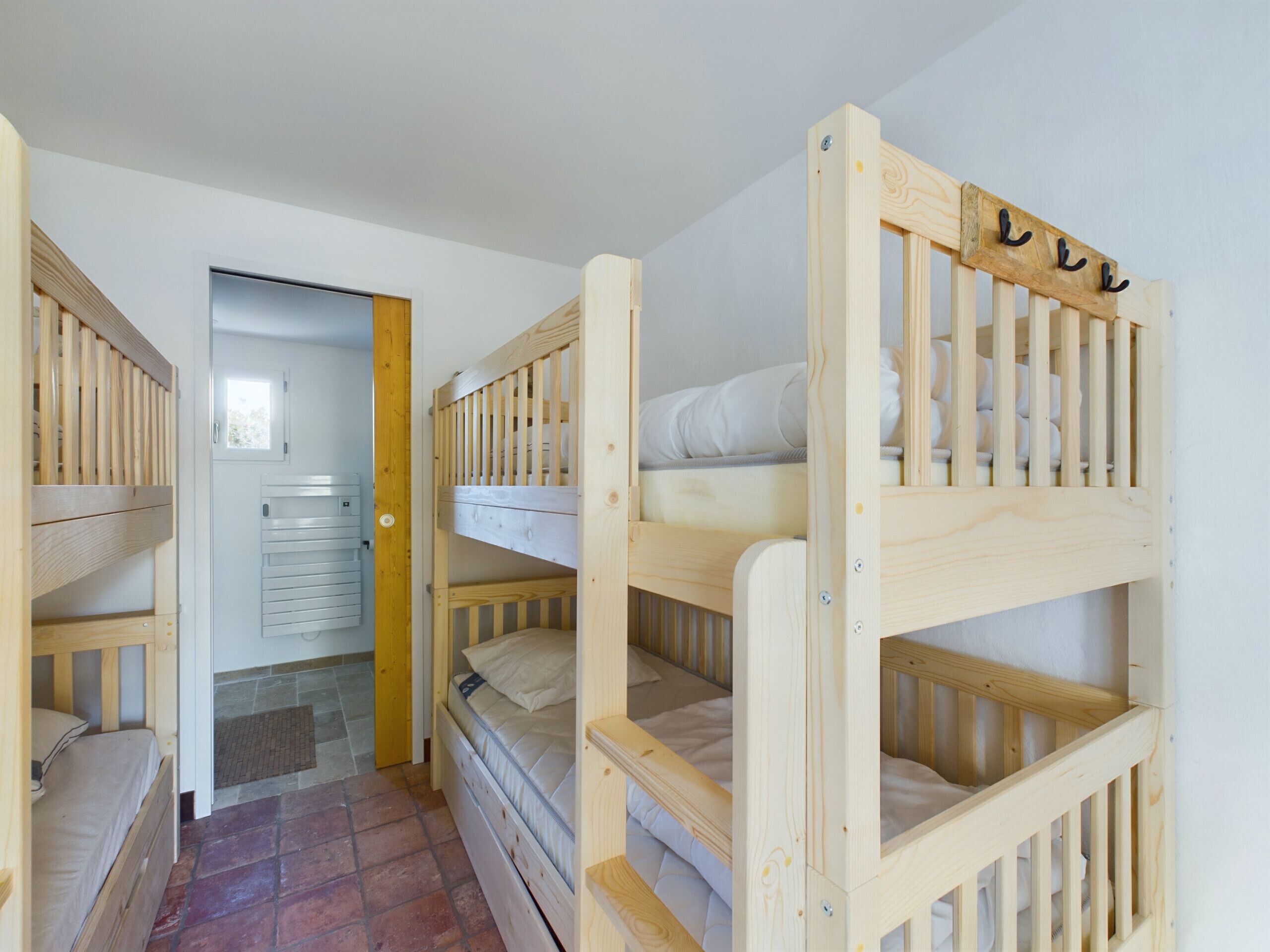 A room with three wooden bunk beds, a door leading to another room, and a radiator on the wall.