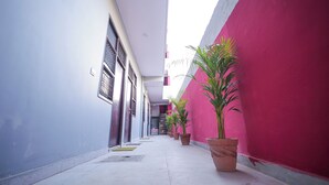 A narrow corridor with a white and pink wall, potted plants, and a door at the end. - Hotel Spark Inn || Near Motherhood Hospital (Noida)