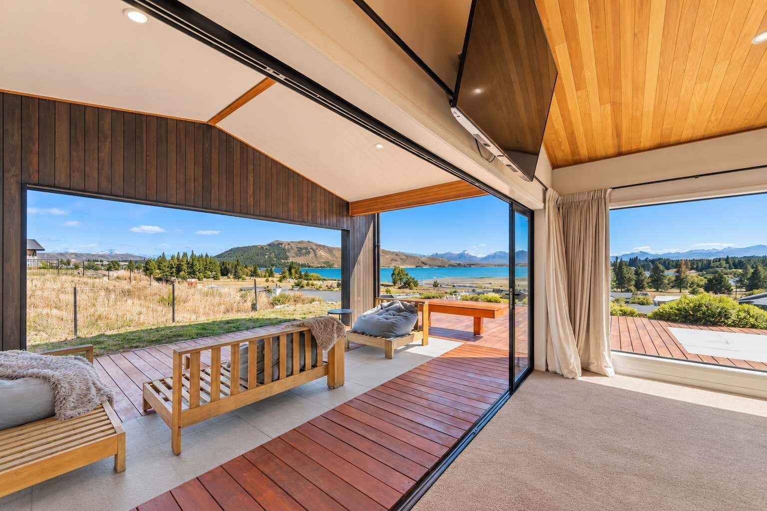A modern interior with a wooden deck, a sofa, and a bench overlooking a scenic landscape.