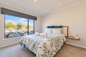 A bedroom with a large window, a bed with floral bedding, and a bedside table with books and a candle.