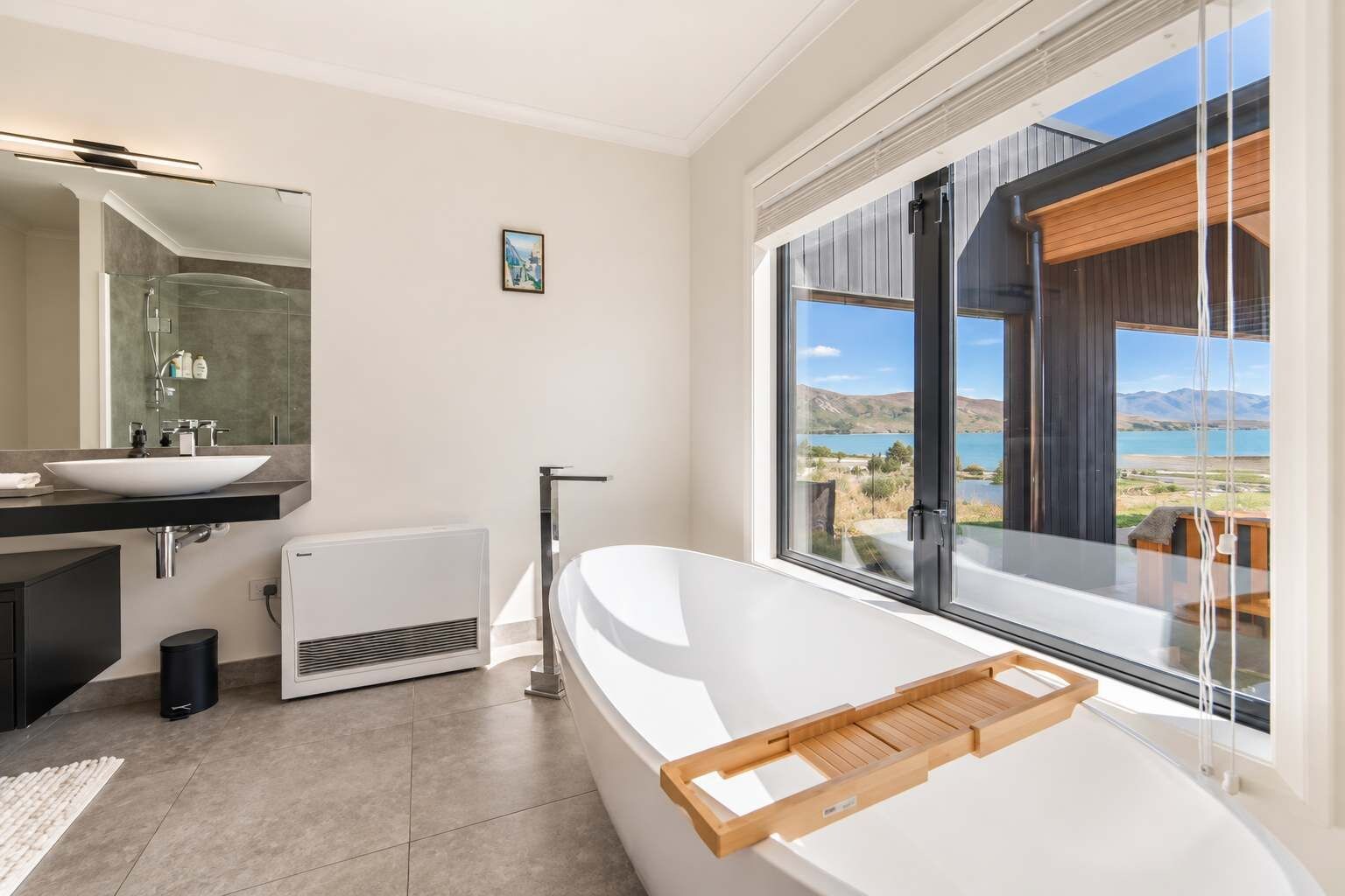 A modern bathroom with a large bathtub, a separate shower area, and a view of a lake and mountains through large windows.