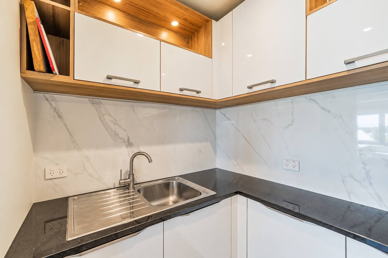 Una cucina moderna con mobili bianchi, un piano di lavoro nero e un lavello in acciaio inossidabile.