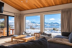 Una sala de estar moderna con un amplio ventanal que ofrece vistas a una montaña nevada y un lago.