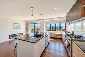 Eine moderne Küche mit einer zentralen Kochinsel, großen Fenstern und Blick ins Freie.