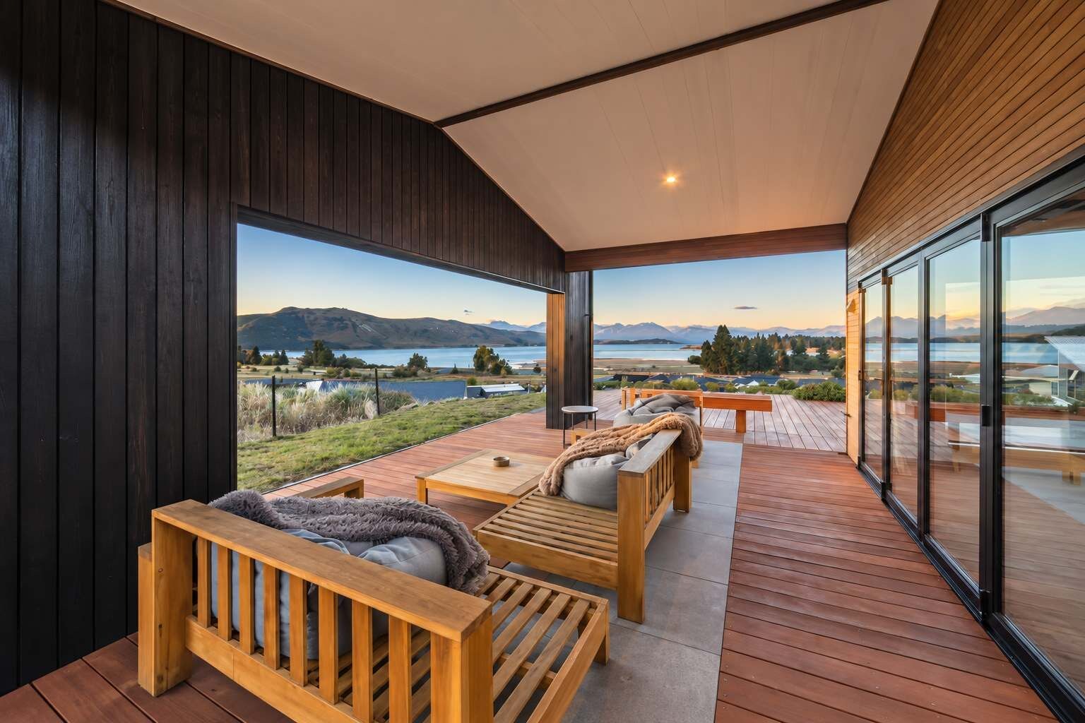 Une terrasse extérieure moderne, dotée de meubles en bois et de portes vitrées, qui offre une vue panoramique sur un lac et des montagnes.
