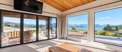 A spacious room with a large sliding glass door leading to an outdoor deck, a wooden ceiling, and a flat-screen TV mounted on the wall.