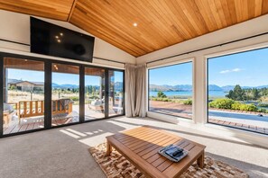 A spacious room with a large sliding glass door leading to an outdoor deck, a wooden ceiling, and a flat-screen TV mounted on the wall. - Cedar Sky | Tekapo 3BR | Near Mt John (Lake Tekapo)