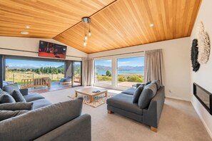 A modern living room with a large window, a sofa set, and a flat-screen TV mounted on the wall. - Cedar Sky | Tekapo 3BR | Near Mt John (Lake Tekapo)