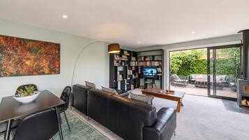 A modern living room with a black leather sofa, a dining table, a bookshelf, and a television.