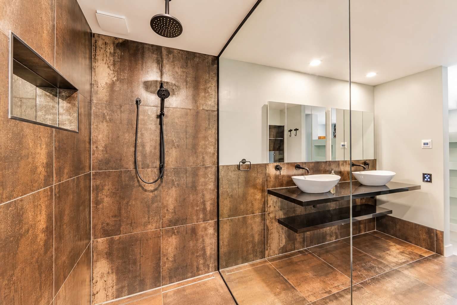 A modern bathroom with a large mirror, two sinks, and a shower.
