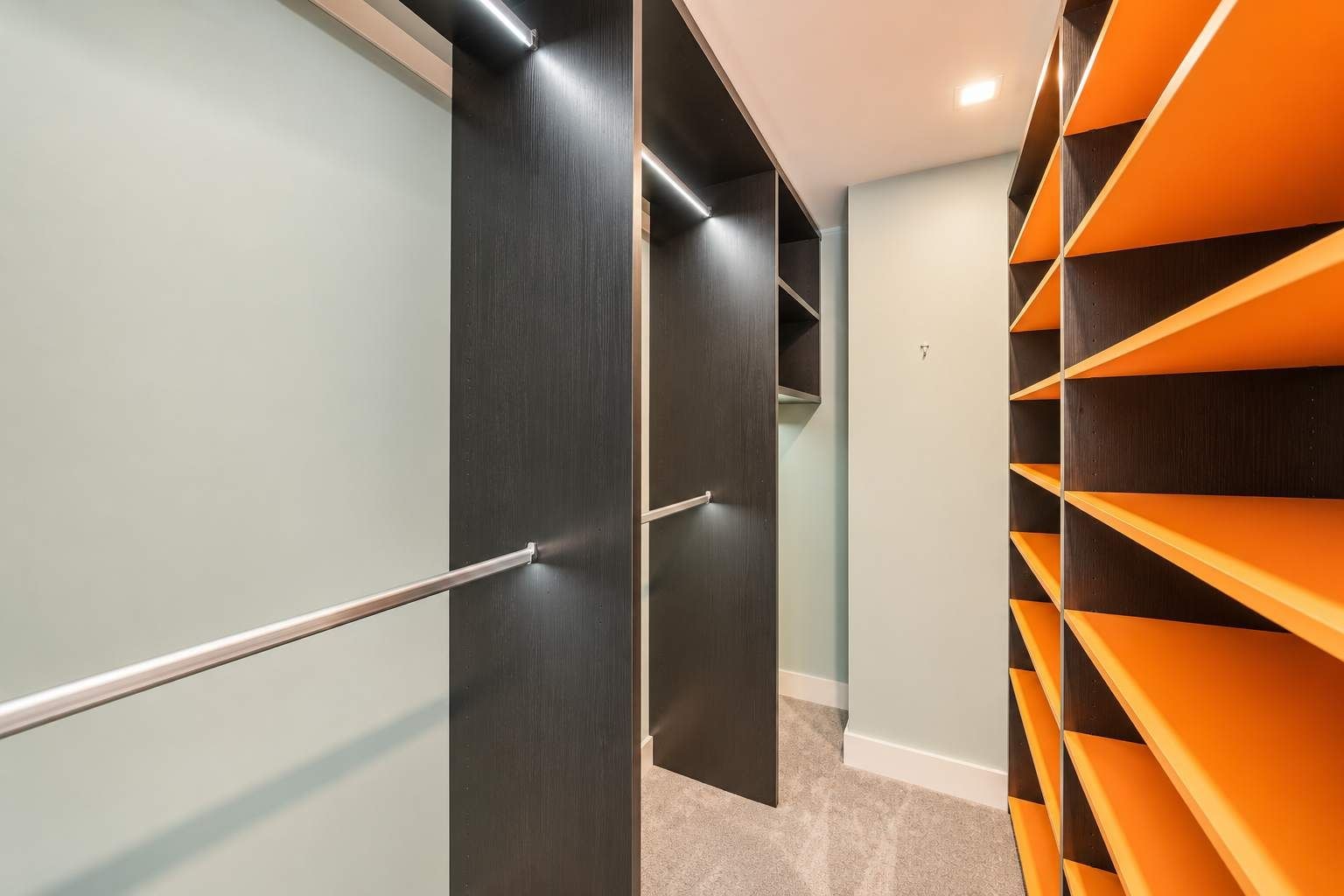 Un placard moderne avec une tringle en métal, des portes en bois foncé et des étagères orange.