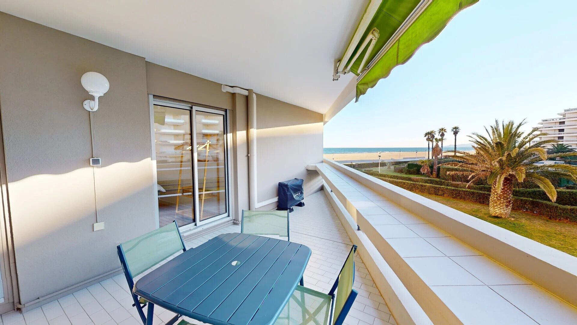 A balcony with a table and chairs, a sliding glass door, and a view of the beach.