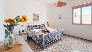 A bedroom with a bed, a hanging light, a window, and a vase with flowers.