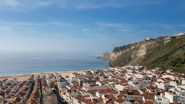 A coastal town with white buildings and red roofs, a beach, and a cliff.