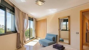 A bedroom with a bed, a chair, a large mirror, and a window with curtains.