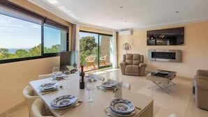 A modern living room with a dining area, large windows, a fireplace, and a TV.