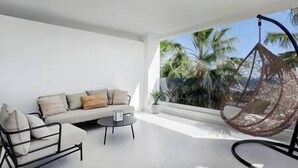 A modern, minimalist living room with a white sofa, a hanging chair, and a small round table. - 2 Bedroom Apartment @Estepona Hills With Sea View! (Estepona)