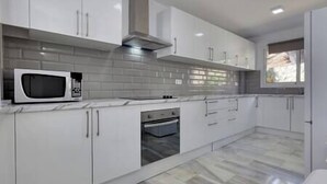 A modern kitchen with white cabinets, a microwave, an oven, and a window.